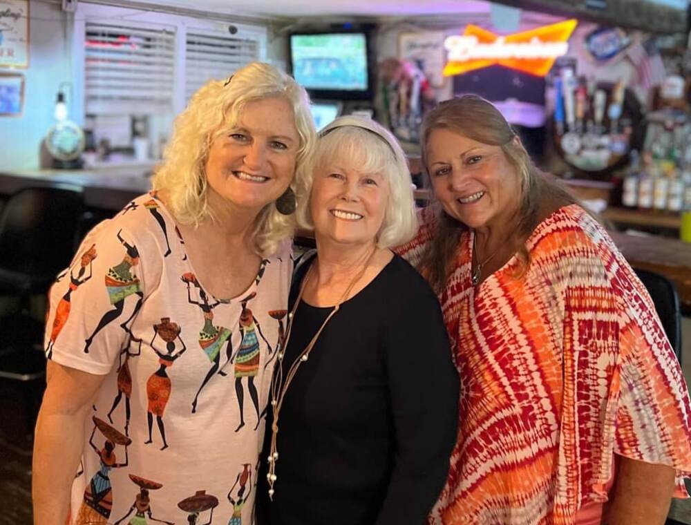 Three friends smiling together at the bar inside The Point Restaurant Perdido